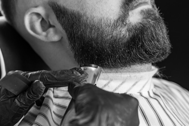 Hombre recortando su barba con maquinilla de afeitar eléctrica en la barbería Imagen en blanco y negro