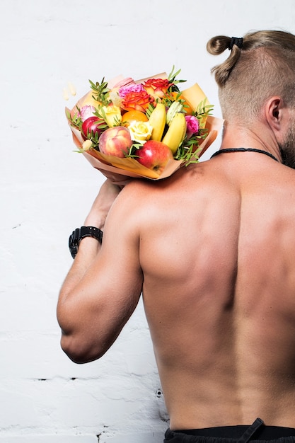 Un hombre regala un ramo de frutas y flores sobre un fondo blanco.