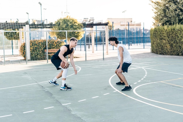 Hombre regateando con una pelota delante de un defensor en un juego de baloncesto entre amigos al aire libre