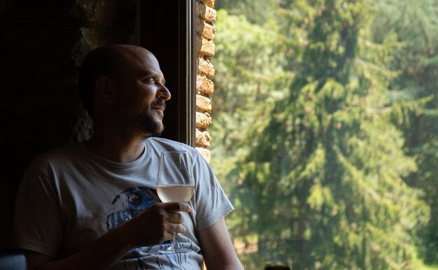 Hombre relajado de mediana edad con una copa de vino blanco en la mano iluminado por una noche oscura