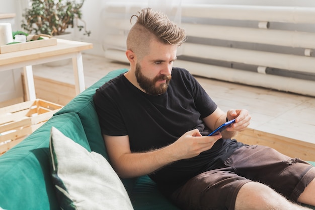 Foto hombre relajado usando un teléfono inteligente sentado en el sofá verde en la sala de estar en casa