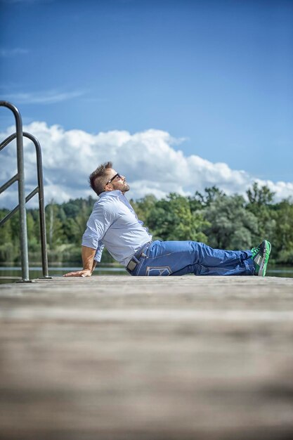 Foto hombre relajándose en el muelle junto al lago contra un cielo nublado