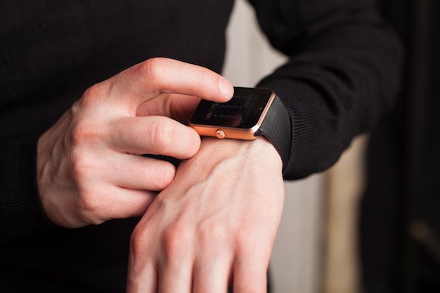 Hombre con reloj inteligente vestido de negro. Cerca de manos.