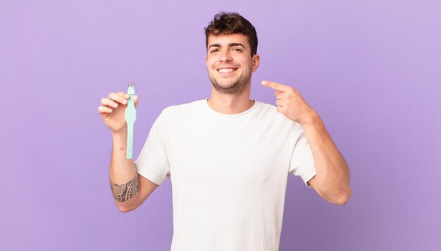 Hombre con un reloj sonriendo con confianza apuntando a su propia sonrisa amplia, actitud positiva, relajada y satisfecha