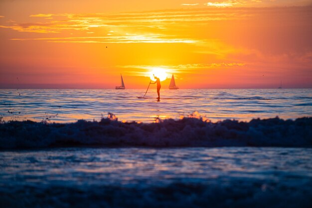 Hombre remando durante un hermoso amanecer. Puesta de sol en el mar. Amanecer en la playa. Salida del sol colorida de la playa del océano.