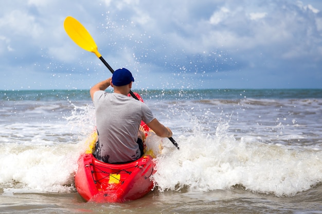 Hombre remando kayak en la ola grande en el mar agitado