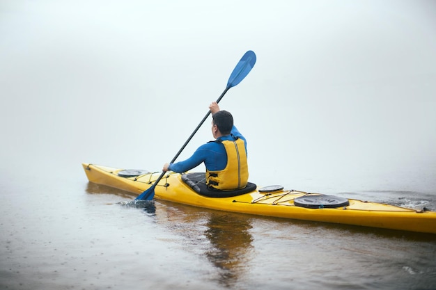 Un hombre remando en kayak en el río brumoso de otoño en la mañana nublada de otoño
