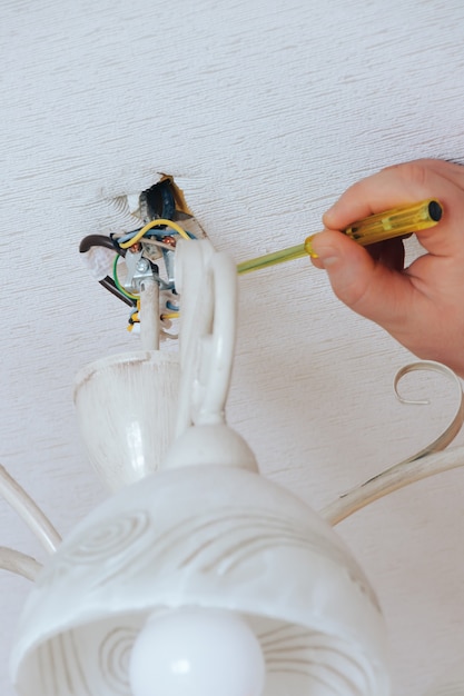 El hombre repara, instala y quita el candelabro blanco con un destornillador en la casa. Servicio de reparación, instalación y remoción de candelabros. Araña desmontada que cuelga con cables expuestos