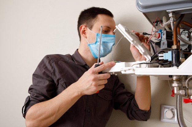 Un hombre reparando una caldera en una máscara médica.