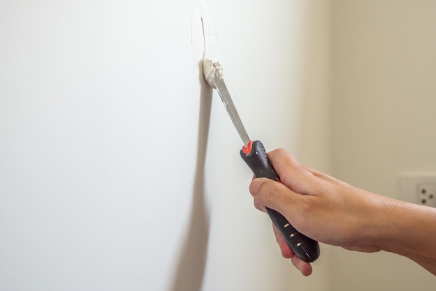 Hombre reparando grietas en la pared blanca con espátula