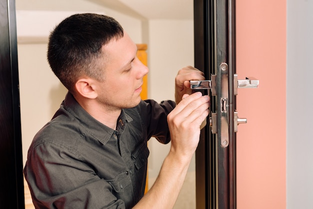 Hombre reparando el pomo de la puerta. Primer plano de las manos del trabajador instalando un nuevo armario en la puerta