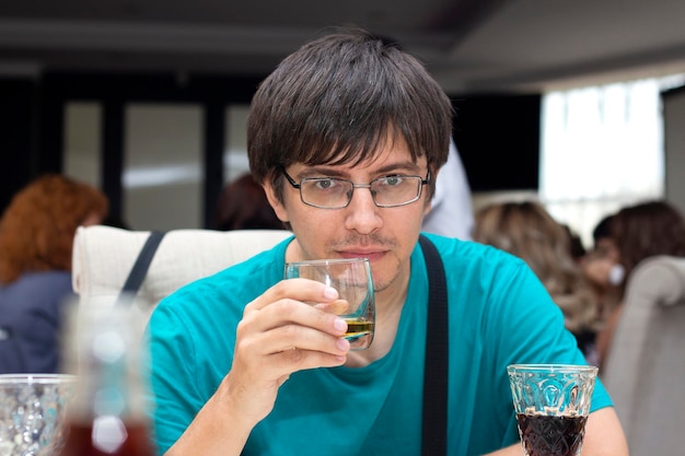 Un hombre en un restaurante sentado en una mesa y sosteniendo un vaso de whisky.