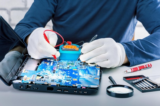 Hombre revisando la computadora portátil. Técnico que usa multímetro para reparar una computadora portátil.