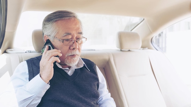 Hombre rico senior de negocios Jugador de bolsa en traje que trabaja con una computadora portátil y usa un teléfono inteligente en su concepto de automóvil para el éxito empresarial senior