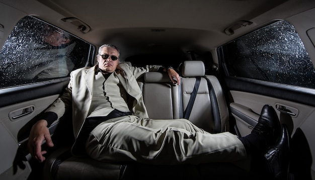 Un hombre rico con un traje blanco y un cigarro en el auto una limusina