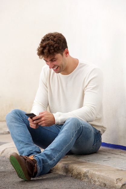 Hombre riendo sentado en el suelo con el teléfono móvil