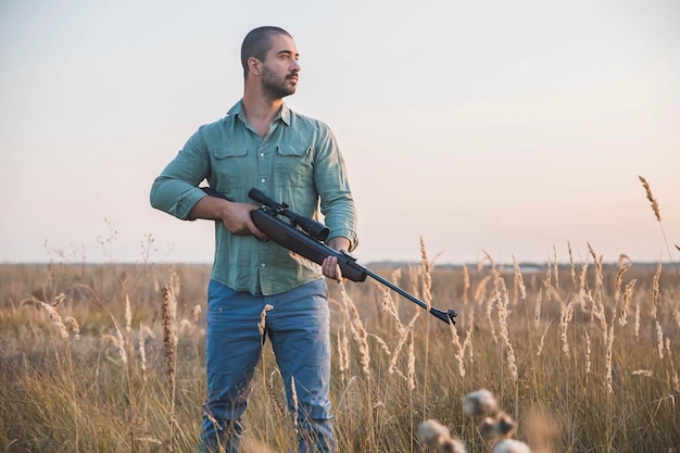 hombre con un rifle con una mira telescópica se encuentra en un campo