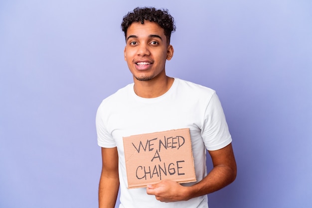 Hombre rizado afroamericano joven aislado sosteniendo un necesitamos un cartón de cambio feliz, sonriente y alegre.