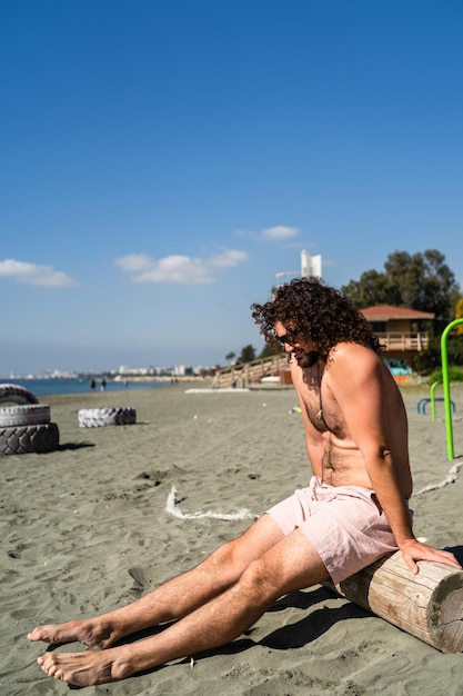 Hombre rizado relajándose en la playa durante el día soleado de verano