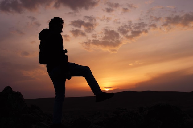 Un hombre se para en una roca frente a una puesta de sol.