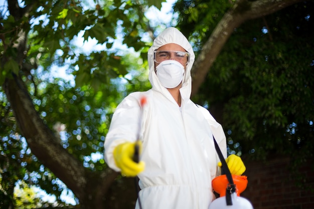 Hombre rociando insecticida mientras está de pie contra el árbol