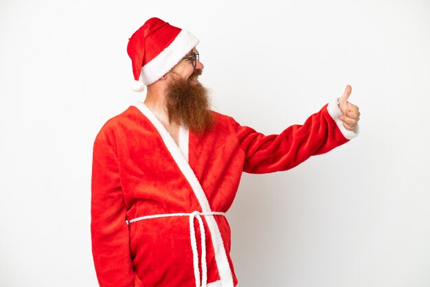 Foto hombre rojizo disfrazado de papá noel aislado en blanco dando un pulgar hacia arriba gesto