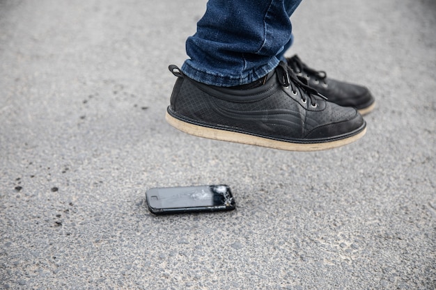 Un hombre rompe el teléfono con el pie en el asfalto