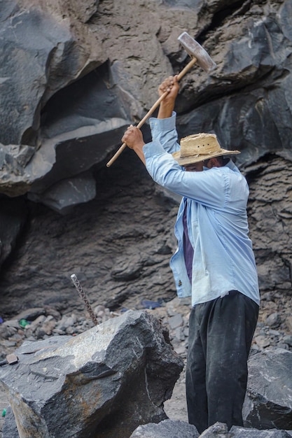 Hombre rompiendo roca volcánica con martillo de metal