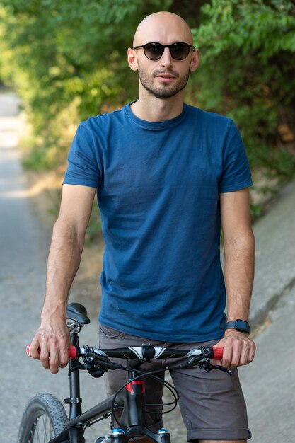 Un hombre con ropa casual está de pie con una bicicleta en un día soleado de verano