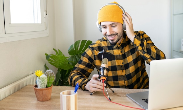 Hombre con ropa clásica y sombrero amarillo sentado en una oficina grabando un programa de radio