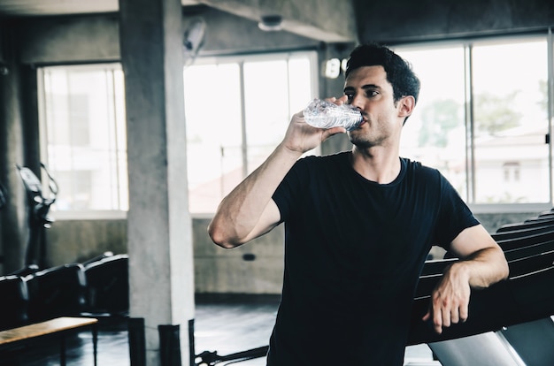 hombre en ropa deportiva corriendo en cinta en el gimnasio y sosteniendo una botella de agua