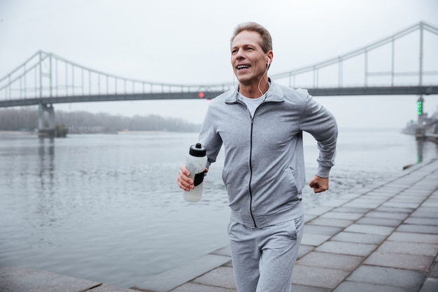 Hombre en ropa deportiva gris con botella de agua cerca del río