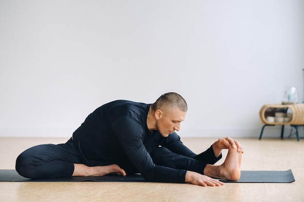 Un hombre con ropa deportiva negra está haciendo estiramientos de yoga en el gimnasio.