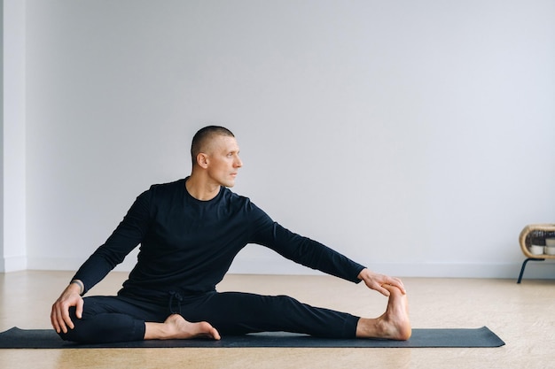 Un hombre con ropa deportiva negra está haciendo estiramientos de yoga en el gimnasio.