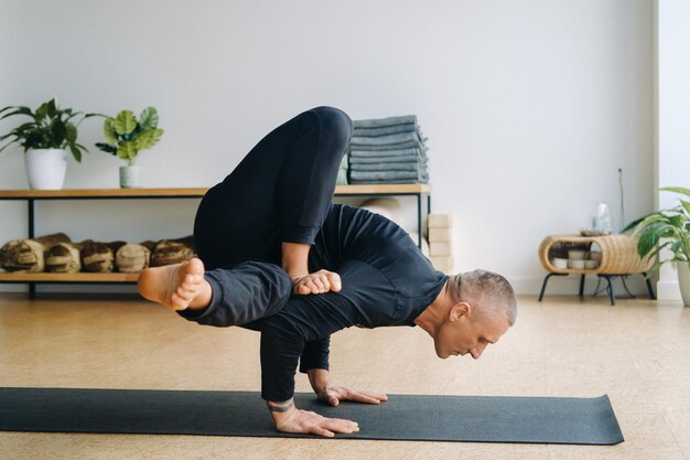 Un hombre con ropa deportiva negra hace yoga parado en sus manos estirándose en el gimnasio