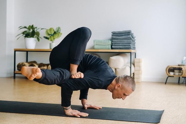 Un hombre con ropa deportiva negra hace yoga parado en sus manos estirándose en el gimnasio