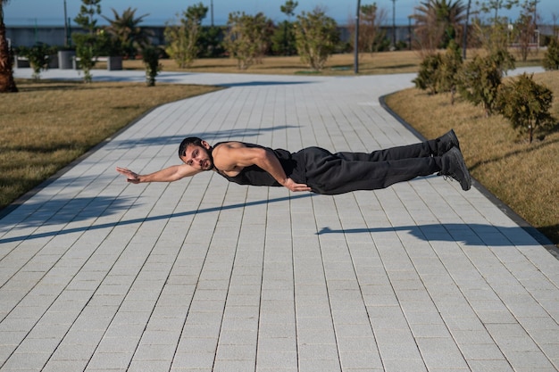 Un hombre con ropa deportiva negra salta haciendo flexiones en el parque