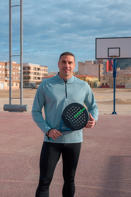 Hombre en ropa deportiva con una raqueta de tenis de paleta mira a la cámara