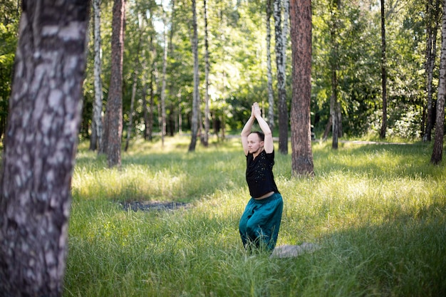 Hombre en ropa deportiva sostiene sus manos desde arriba mientras practica yoga en la naturaleza entre los árboles