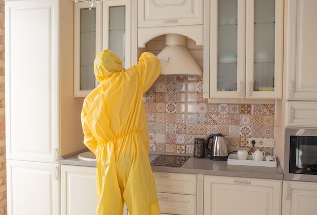 Un hombre con ropa especial de protección limpia y realiza limpieza sanitaria en el apartamento.