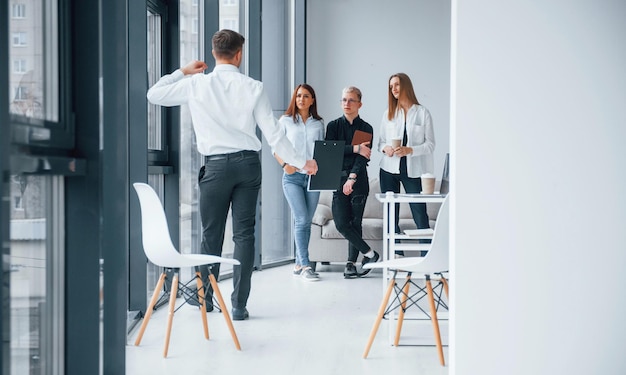 Hombre con ropa formal caminando y hablando Grupo de jóvenes equipos exitosos que trabajan y se comunican juntos en el interior de la oficina