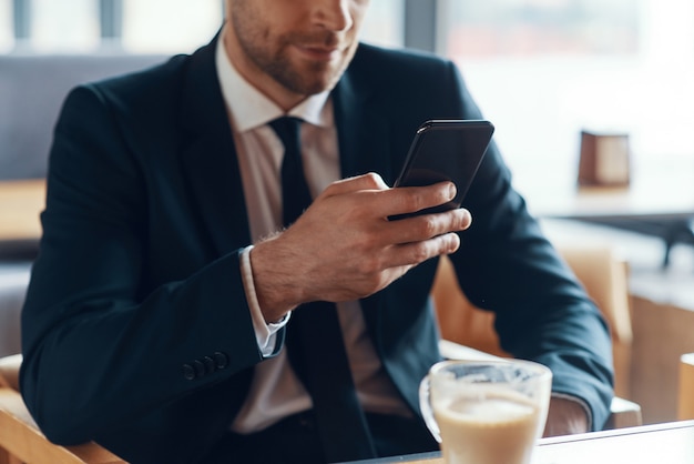 Hombre en ropa formal con teléfono inteligente mientras está sentado en la cafetería