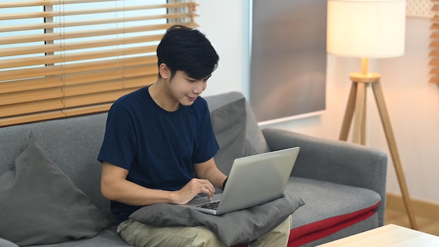 Hombre con ropa informal sentado en la cama y revisando el correo electrónico o trabajando en línea con una computadora portátil