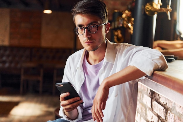 Hombre con ropa informal sentado en el pub con el teléfono en la mano