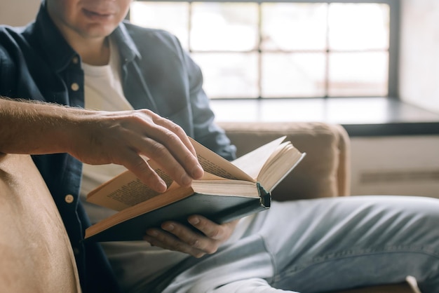 Hombre con ropa informal sosteniendo un libro en sus manos cerca del fondo de una ventana con espacio