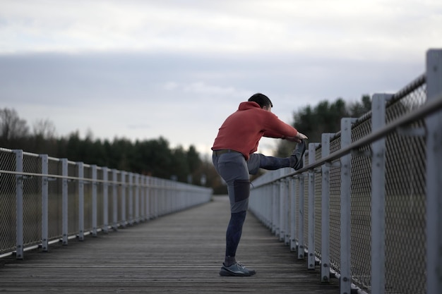 Hombre con ropa naranja y cálida calentándose antes de correr al aire libre en el frío clima otoñal en b de madera