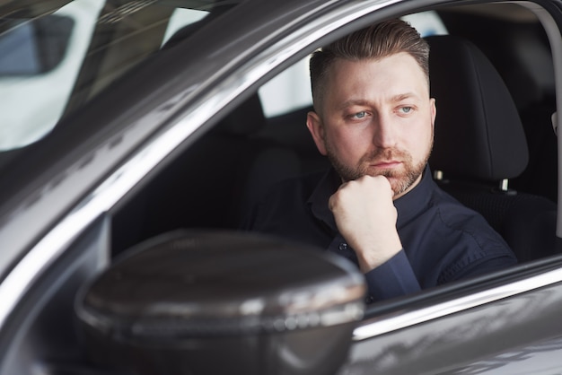 Hombre en ropa oficial probando su nuevo coche en el salón del automóvil