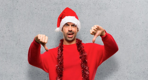 Hombre con ropa roja celebrando las fiestas navideñas mostrando pulgar hacia abajo