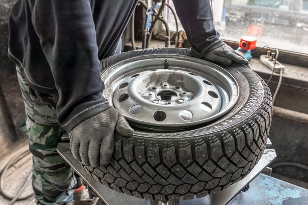 un hombre con ropa de trabajo y guantes repara un automóvil se pone neumáticos de invierno