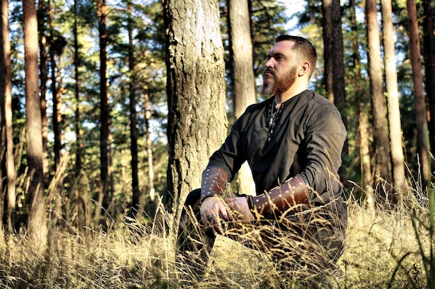 Foto hombre con ropa tradicional arrodillado en el campo contra los árboles